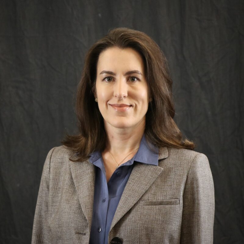 Image of a woman with shoulder-length brown hair wearing a gray blazer and blue shirt